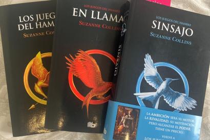 Tres libros en una cama. Son en espanol. Los titulos son "Los Juegos de Hambre," "En Llamas," y "Sinsajo."