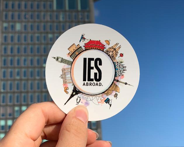 an IES Abroad logo sticker being held up to the sky