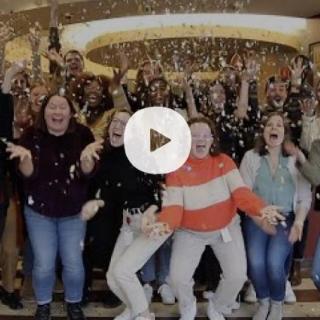 staff throwing confetti in the air with a play button superimposed
