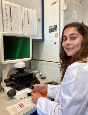 student in white coat sitting at desk in front of microscope and computer
