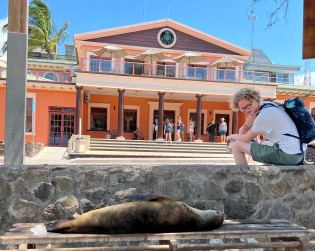 a student sitting new the GAIAS building looking at a sealion laying on a bench