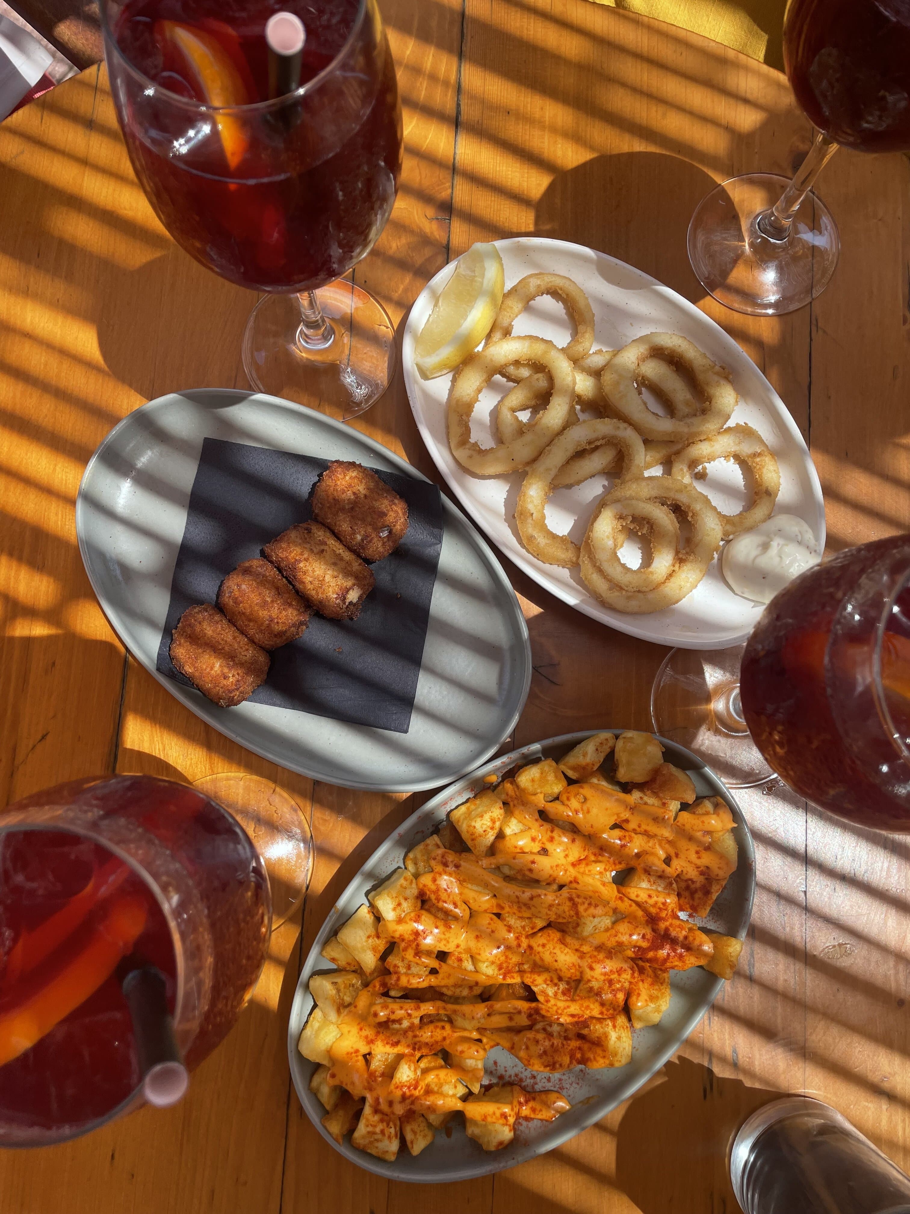 four glasses of Tinto de Verano and three plates of tapas: croquetas, calamari, and patatas bravas.