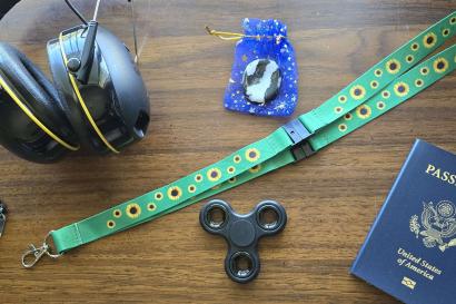 A pair of construction headphones, a medical bracelet, a sunflower lanyard, a worry stone, a fidget spinner, and a passport sitting on a table.