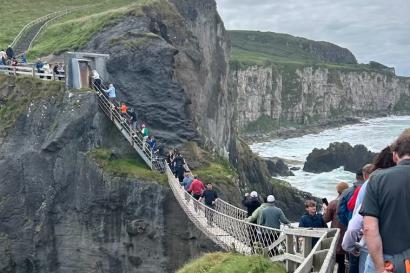 The view from the second side of the rope bridge - visible is people on the bridge and waiting on either side, as well as the cliffs around and behind.