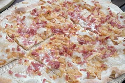 A picture of a standard flammkuchen, a thin pizza with bacon and onions and a creme sauce adorning it.