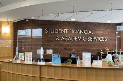 Front view of the Brandeis Student Financial Services reception desk, with a sign behind it reading 'Student Financial and Academic Services'