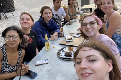 Selfie of a large group of students sitting outdoors at a long, white table 