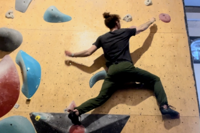 Photo of Tal on a bouldering wall, jumping horizontally to reach the next climbing hold. 