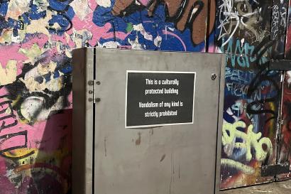 Photo of a sign prohibiting vandalism of any kind, directly in front of a graffiti-covered wall