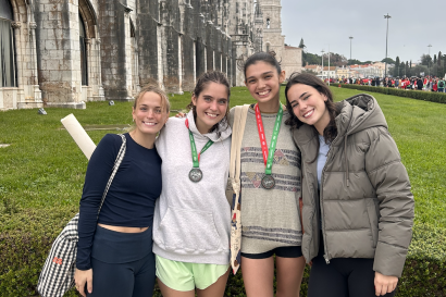 Four girls standing in front of a Lisbon monument. Two have just run a half marathon, the others are holding signs to cheer for them. 