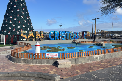 Sign that says "San Cristobal" with an island map display with a Christmas tree and ocean in the background. 