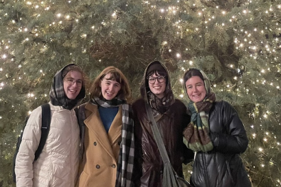 Four students pose in front of a large Christmas tree, bundled up in winter clothes. 