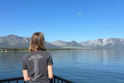 Image of the author facing away from the camera, looking out over a lake with a small yellow hot air balloon in the distance.