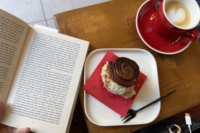 Picture of a cappuccino cinnamon roll, and open book at Specialty Milano