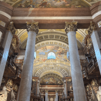 The Grand Hall of the Austrian National Library which has giant marble pillars and a beautiful mural of angels and other figures on the ceiling.