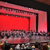 A youth orchestra on a stage with red lighting.