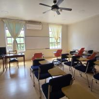 A classroom with a wood floor, white walls, open windows, and rows of desks.