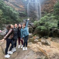 A group of friends posing in front of a waterfall at the Blue Mountains. 