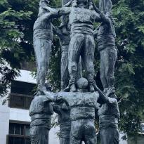 A metal statue of human towers where individuals build off one another to resemble a tall tower. 