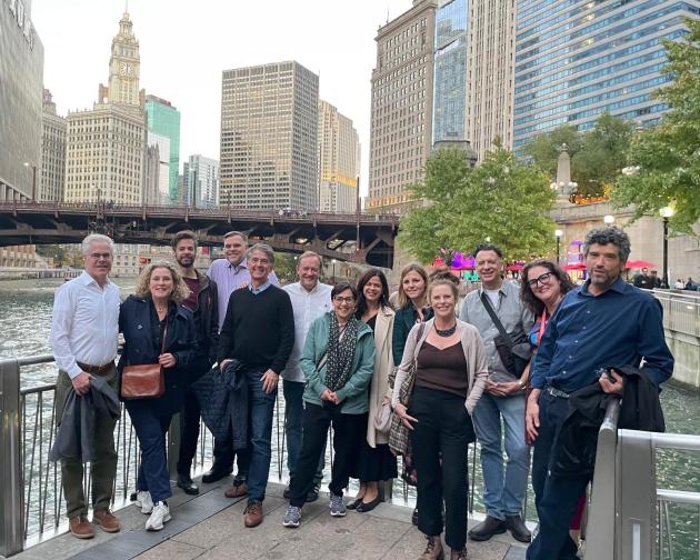 group of staff standing in front of a river, bridge, and large tall buildings