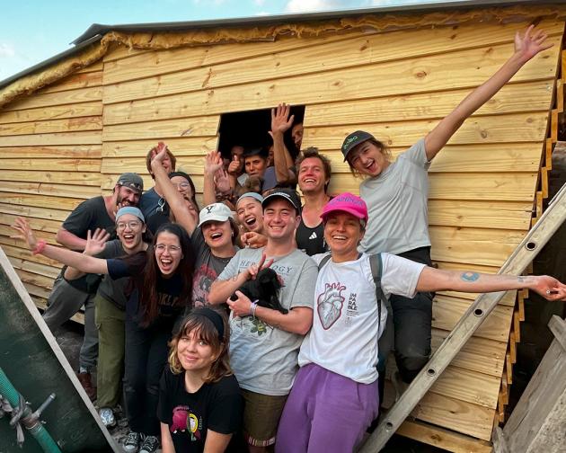 a group of students pose for a photo with a transitional home they built for a family in need