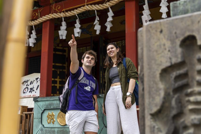 two students standing in front of decorated building pointing and smiling