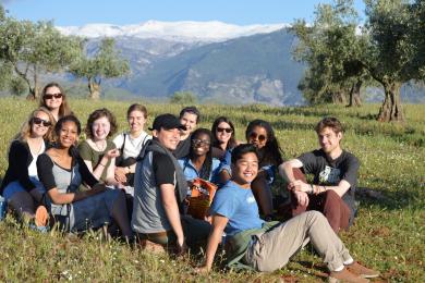 large group of people sitting in grassy area in front of trees and mountains