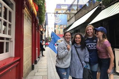 four students standing in front of train holding up gaelic dublin football flag