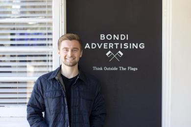 student standing in front of sign that reads "bondi advertising think outside the flags"