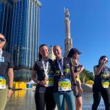 Two girls smile in front of a fountain and a statue. They are wearing bibs for a running race and medals.