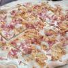 A picture of a standard flammkuchen, a thin pizza with bacon and onions and a creme sauce adorning it.