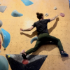 Photo of Tal on a bouldering wall, jumping horizontally to reach the next climbing hold. 