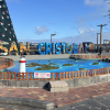 Sign that says "San Cristobal" with an island map display with a Christmas tree and ocean in the background. 