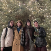 Four students pose in front of a large Christmas tree, bundled up in winter clothes. 