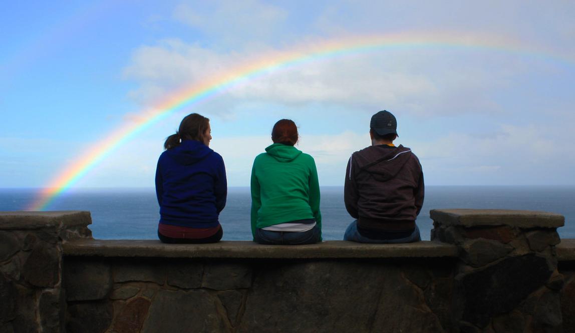 students sitting by the sea in Australia with a rainbow over them