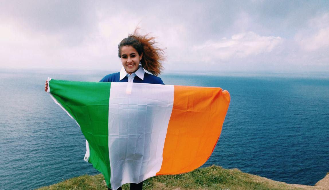 dublin student holding an Irish flag at the Cliffs of Moher
