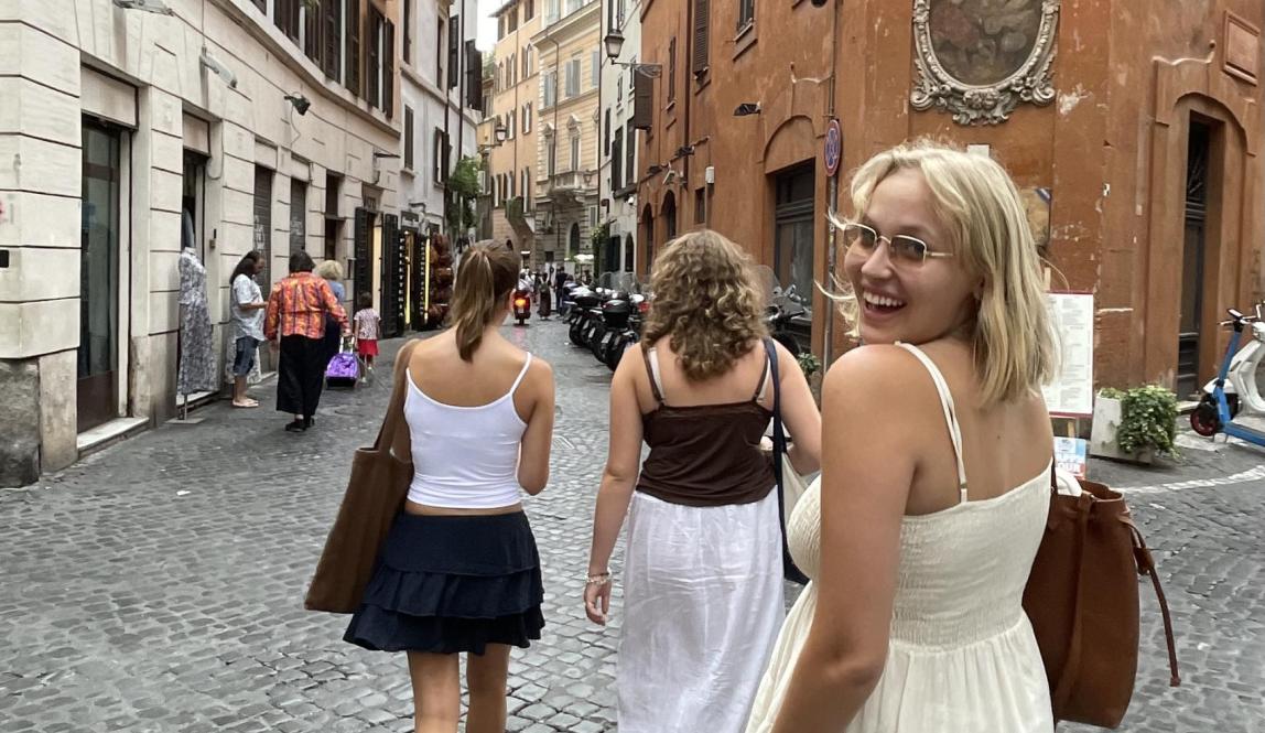 three students walking down a stone road in rome near brick buildings