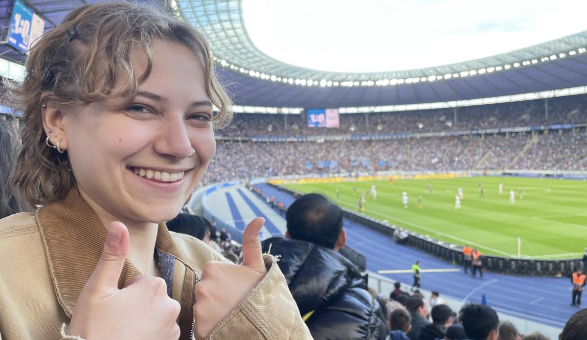 A young woman gives a thumbs-up in front of the Olympiastadion in Berlin