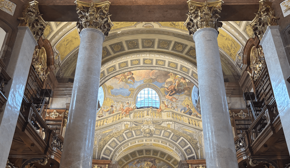The Grand Hall of the Austrian National Library which has giant marble pillars and a beautiful mural of angels and other figures on the ceiling.