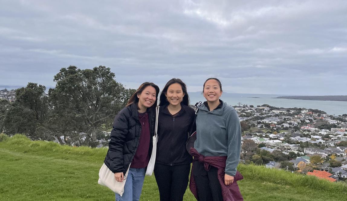 Three girls pose on Takarunga or Mount Victoria. The sky is cloudy and dark in the background.