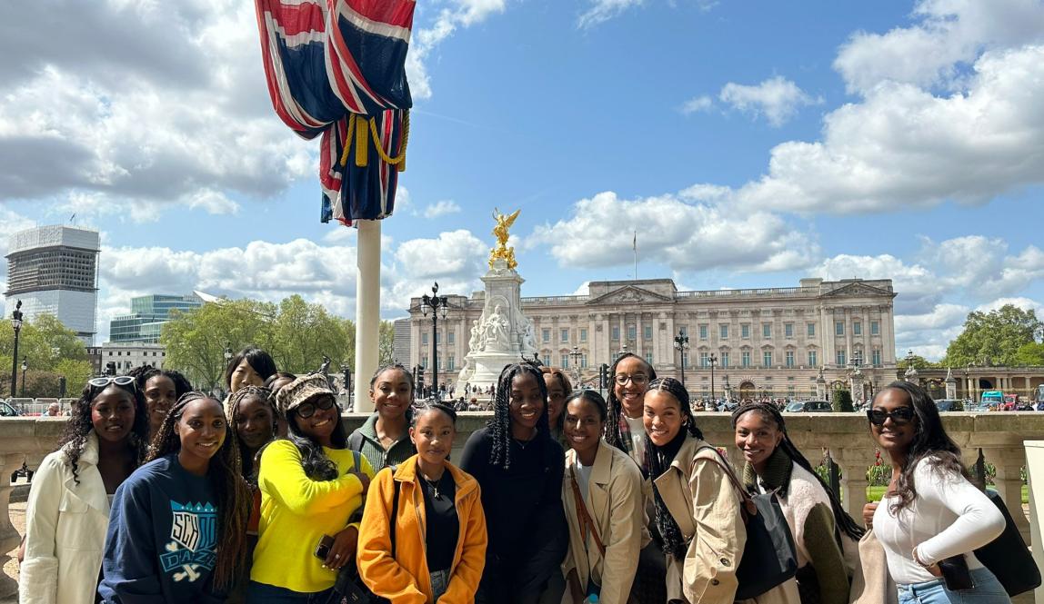 group of london students standing next to british flag in front of buckingham palace