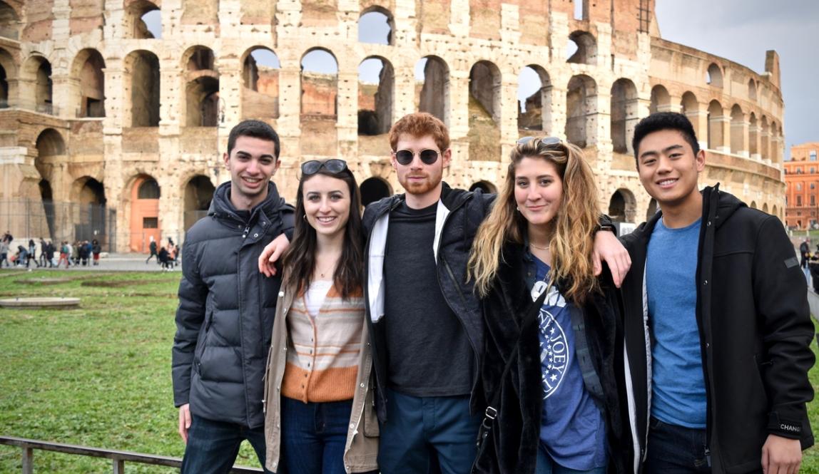 A group of students stand together, smiling with the Colosseum behind them.