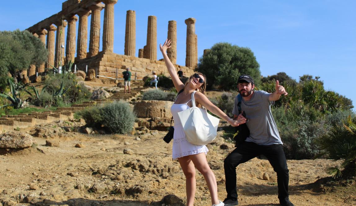Two students stand in front of ancient Roman ruins, striking fun poses and smiling.