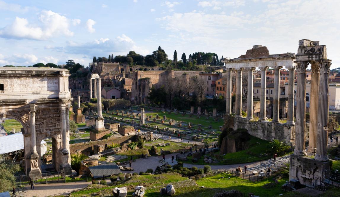A view of the Roman forum, ancient Roman ruins and open green space.