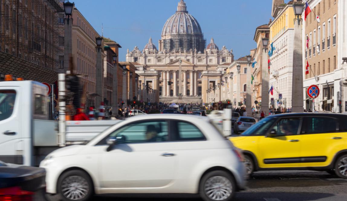 A timelapse photo of a busy street in front of the Vatican in Rome, with cards driving in front of the iconic building.