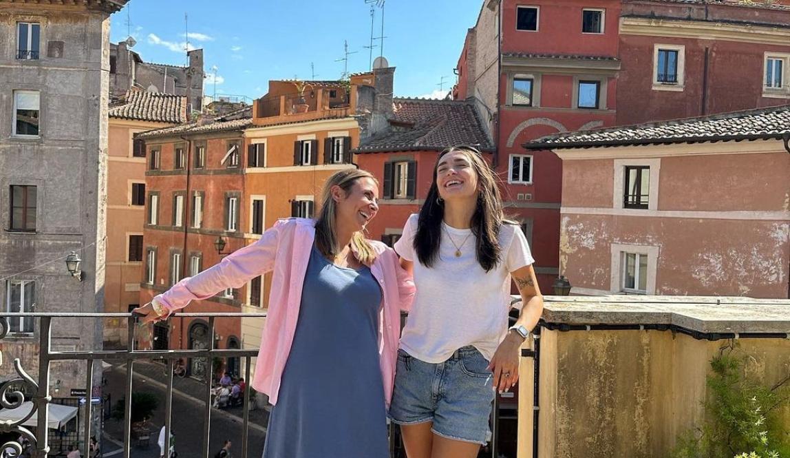 Two students stand next to eachother laughing on a sunny rooftop in Rome.