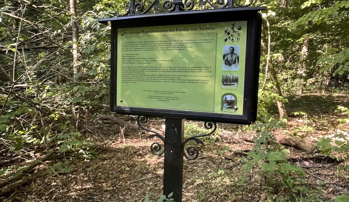 A sign with German text on it stands along a trail through the woods