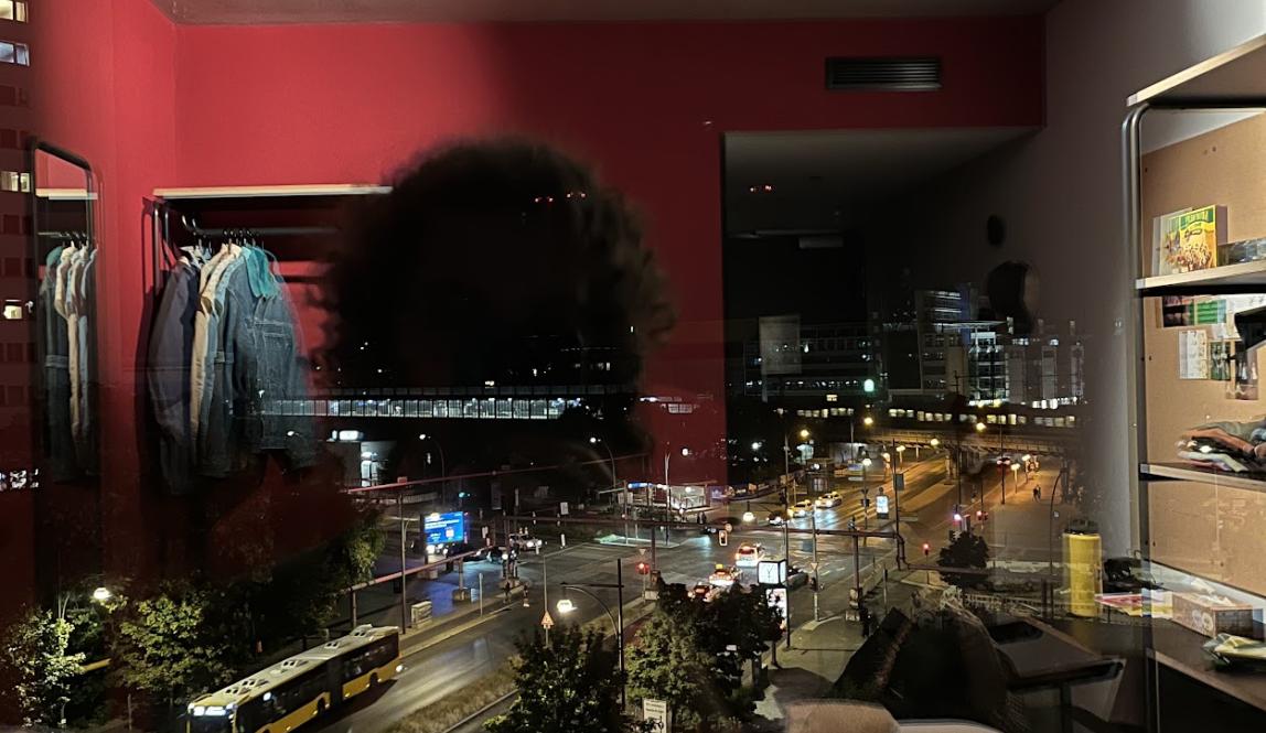 View out the window at night; the busy street outside can be seen at the same time as a reflection of the bedroom inside