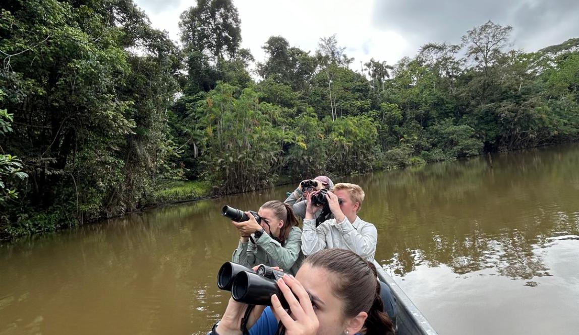 Picture of individuals in a small boat using binoculars and cameras to look at something. 