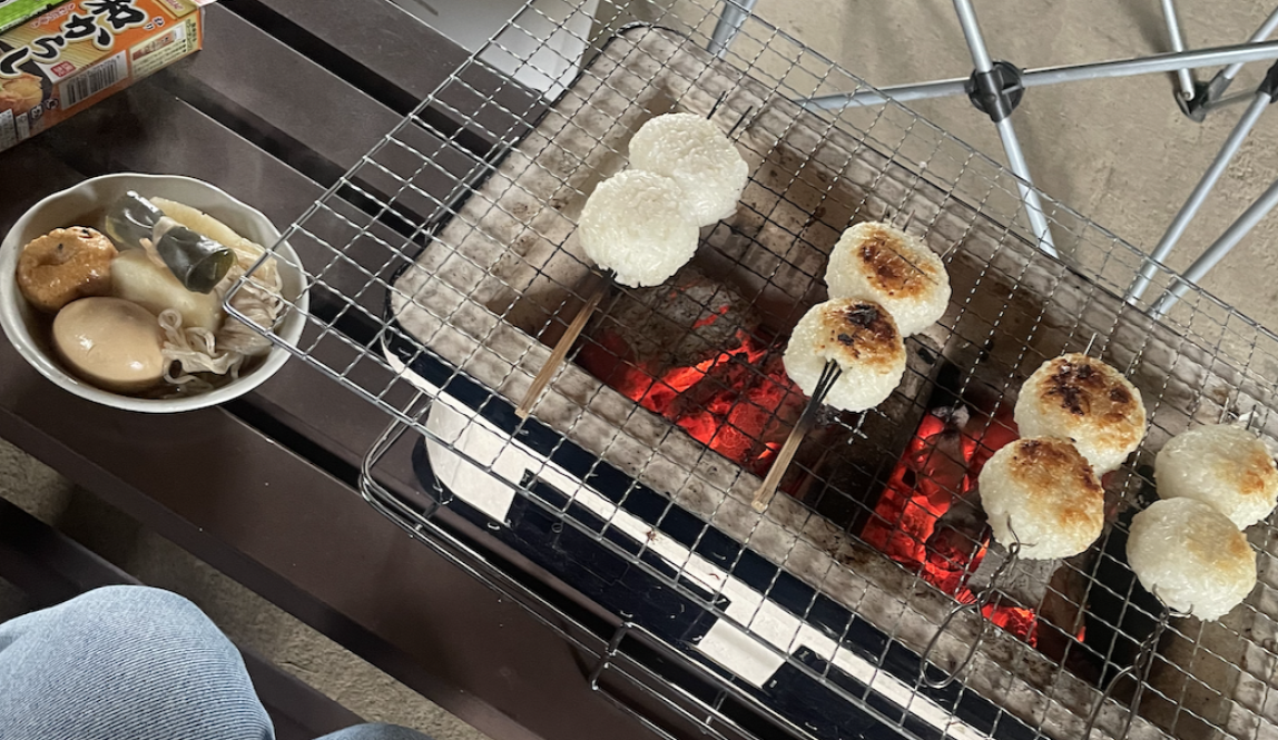 Rice balls roasting over a grill on a stick, with a side of oden.